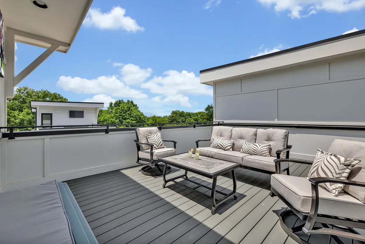 A stylish outdoor seating area with a coffee table and lush green trees in the background. The tranquil setting suggests a comfortable space for relaxing or socializing with friends, embodying leisure and upscale comfort.