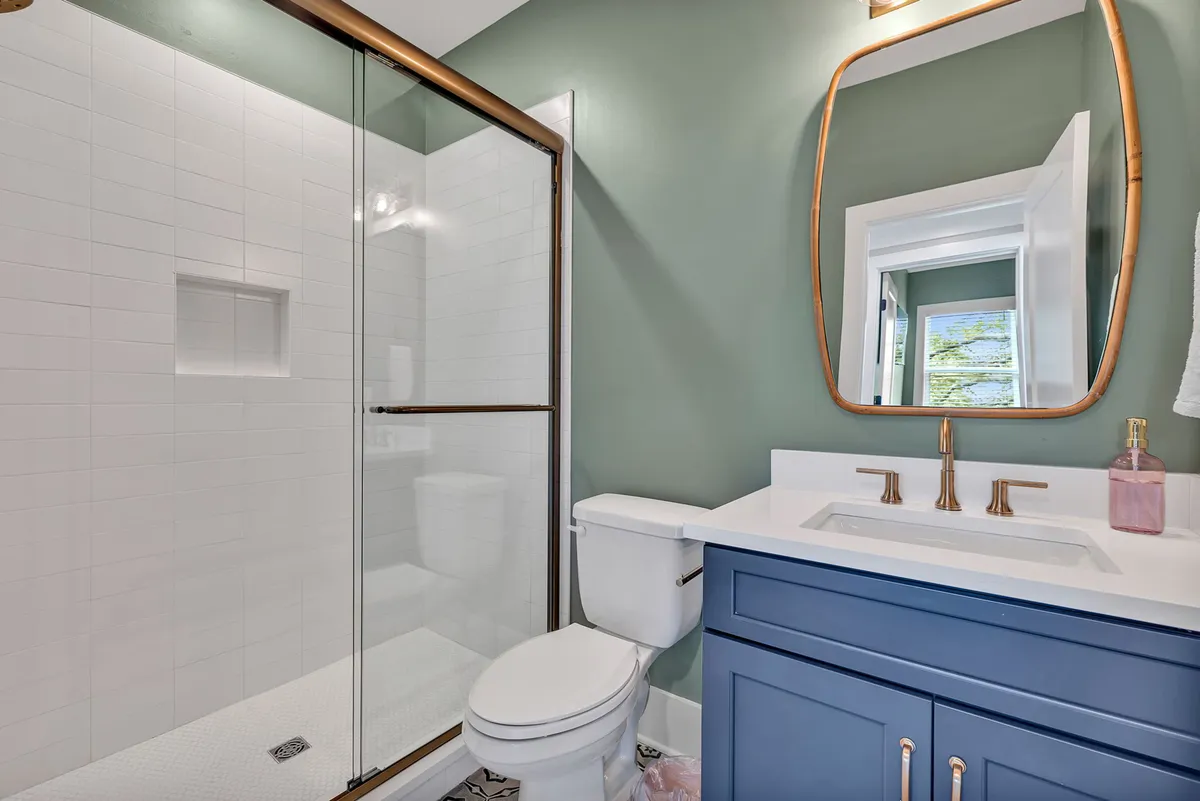 A serene bathroom featuring a glass shower enclosure, blue vanity, gold fixtures, and a large mirror. The design is contemporary, with clean lines and a refreshing atmosphere ideal for unwinding after travel.
