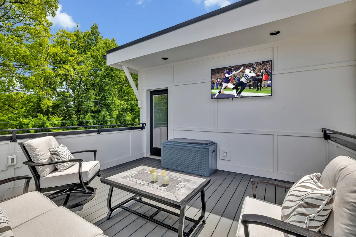 An elegant rooftop space with comfortable seating, a coffee table, and an outdoor television. The view extends to the city beyond, creating a seamless blend of cozy relaxation and urban excitement. The mood is casual and welcoming, ideal for group activities or quiet evenings.