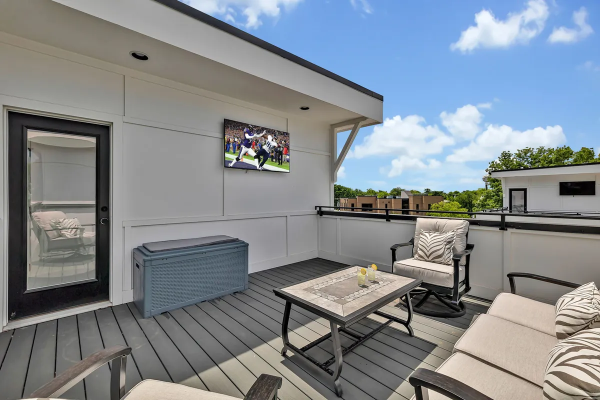 This image features a stylish rooftop seating area with plush outdoor furniture, a decorative table adorned with candles, and a large television, all set against an open sky. The ambiance is relaxed and inviting, perfect for entertaining guests, enjoying drinks, or watching a game outdoors.