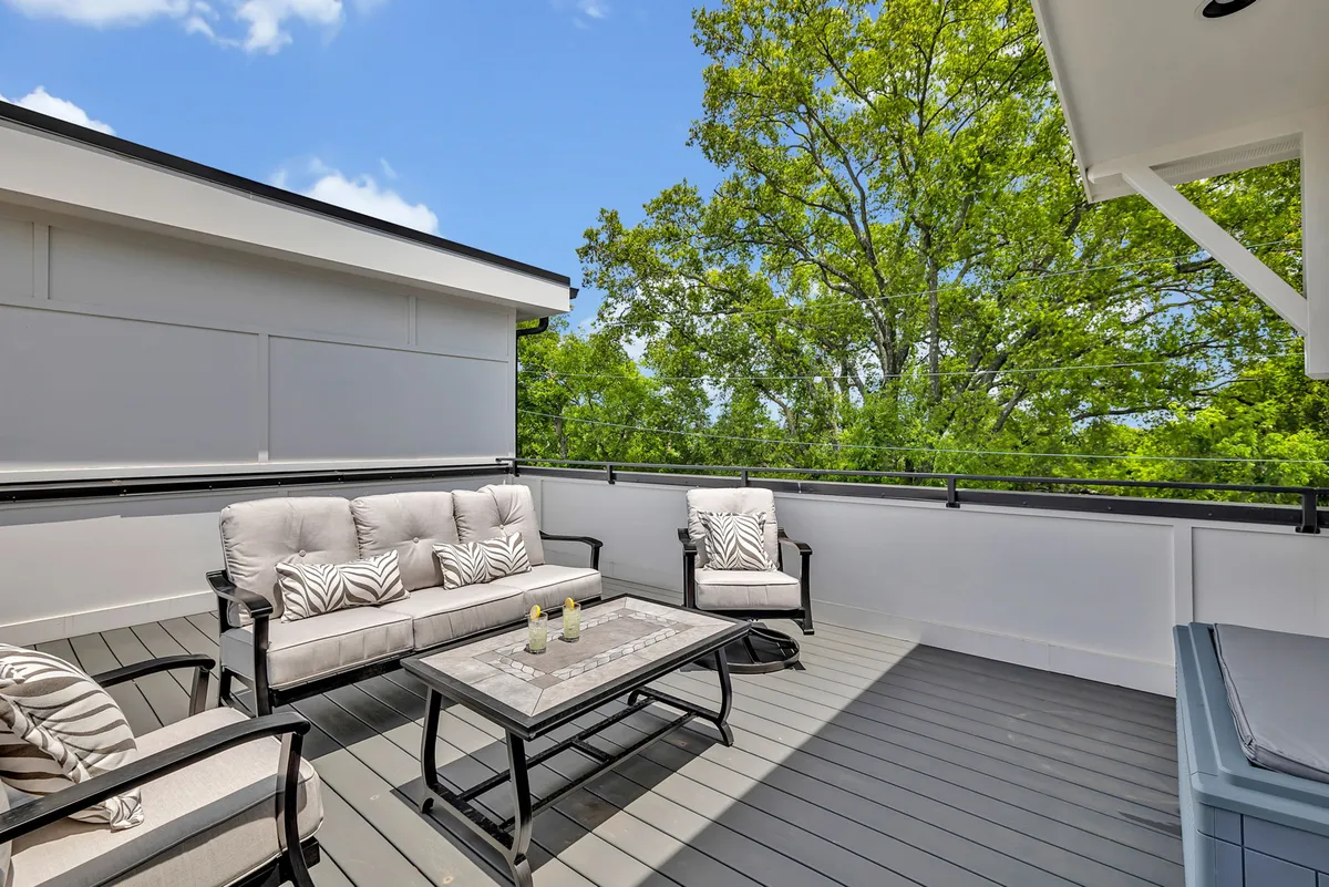 A cozy, well-appointed rooftop deck with comfortable seating, decorative cushions, and a coffee table set against the open sky. The setup suggests a perfect place for evening cocktails, sunset views, or late-night laughter under the stars.